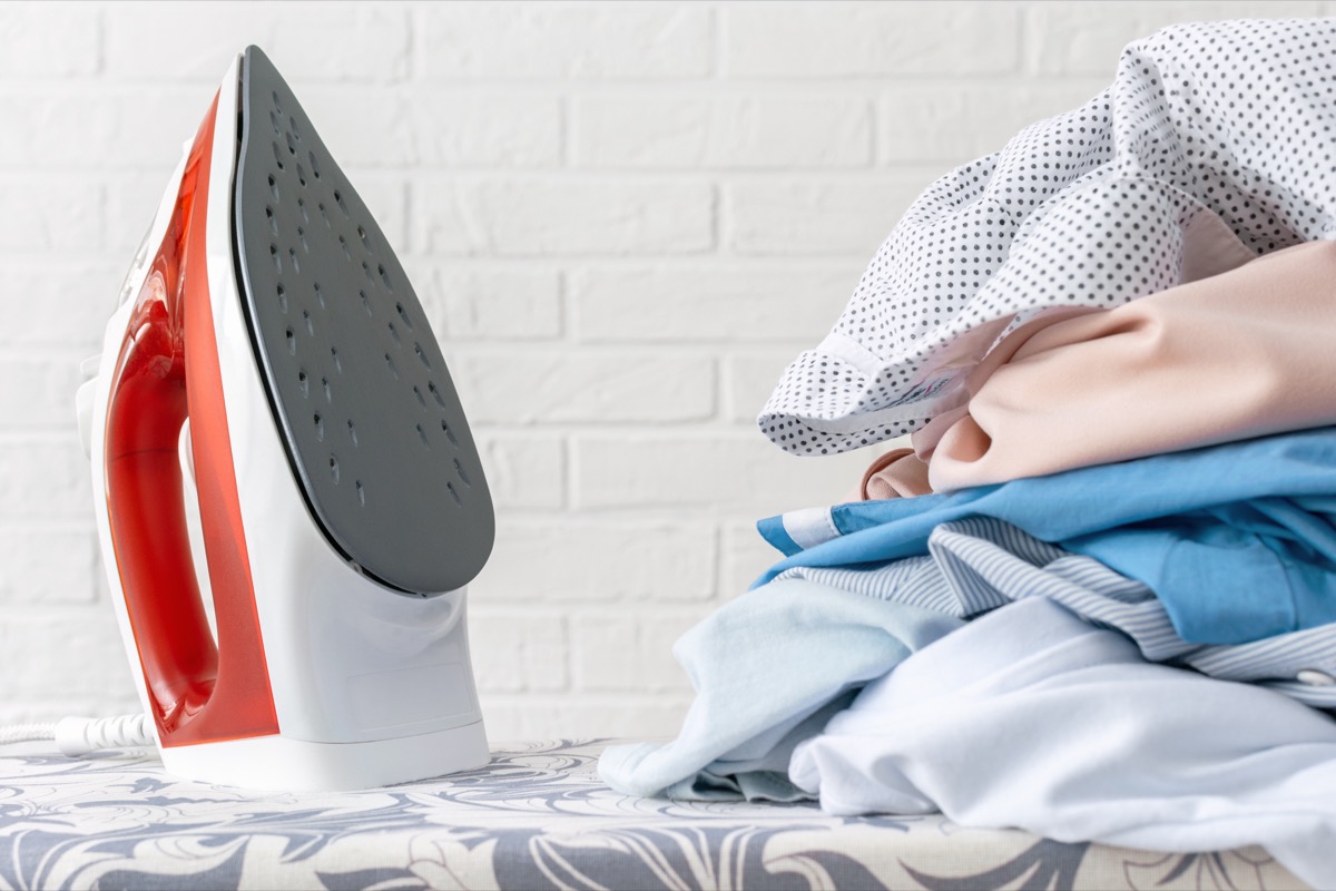 Iron and neatly folded clothes on ironing board — ironing and pressing service